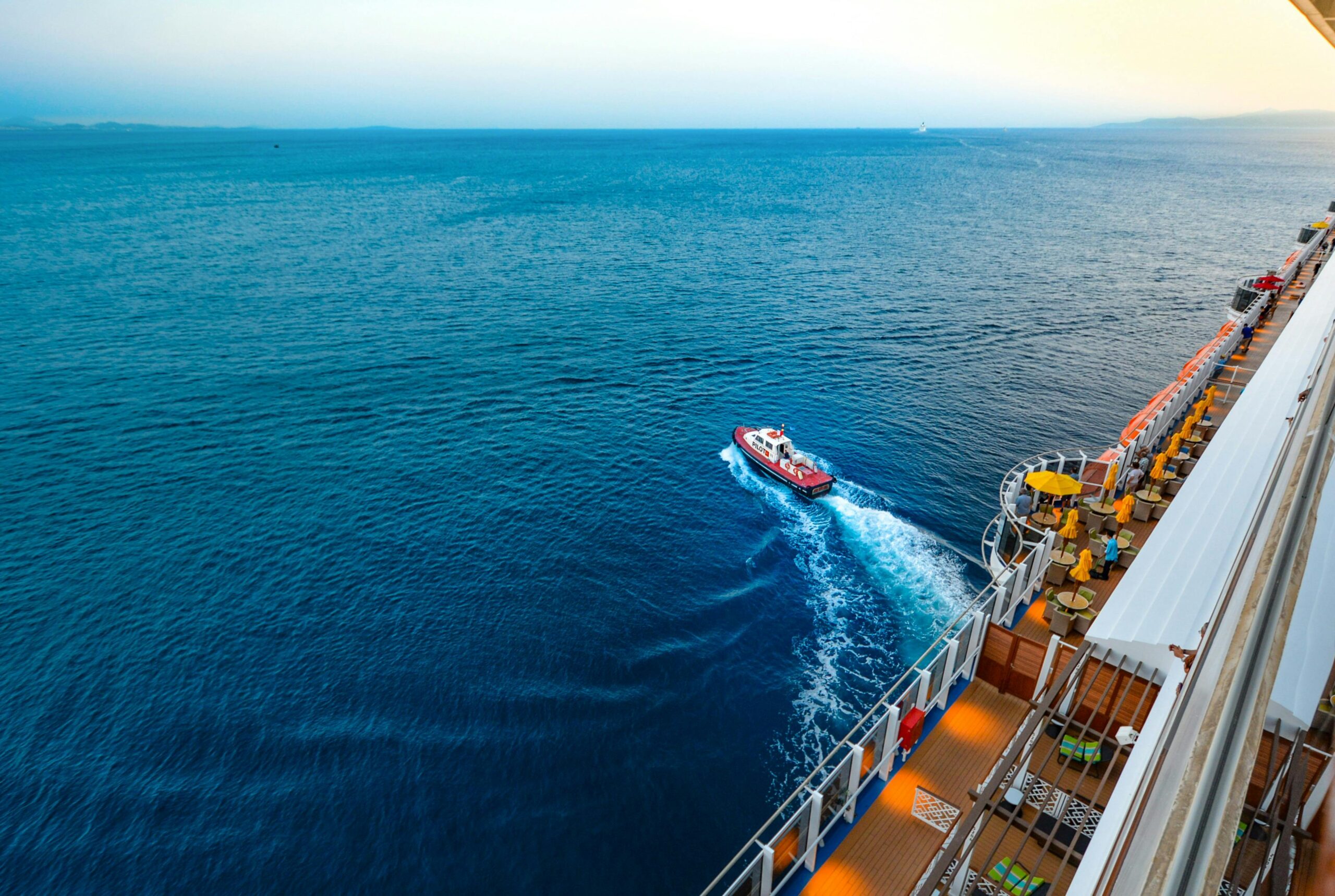 Blog Aerial view of a luxury cruise ship with a small boat on a vast ocean at sunset.